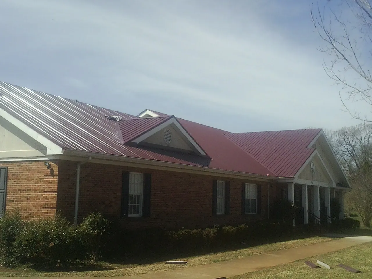 Red metal roof with gabled entries on a long brick building, from a Hail Damage Roof Repair job in Burgettstown
