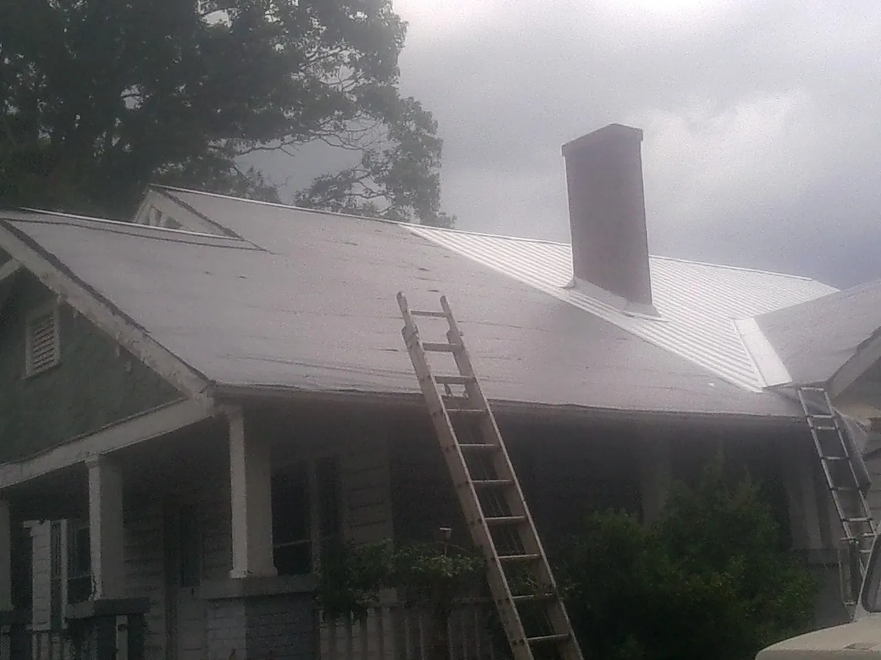 Ladders against a metal roof on an older home with a brick chimney in Burgettstown