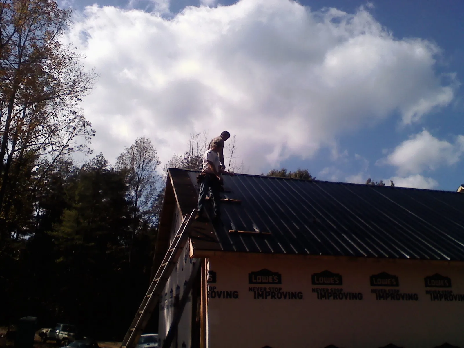 Roofer fastening dark metal panels high against a cloudy sky, from a Roof Inspection job in Burgettstown