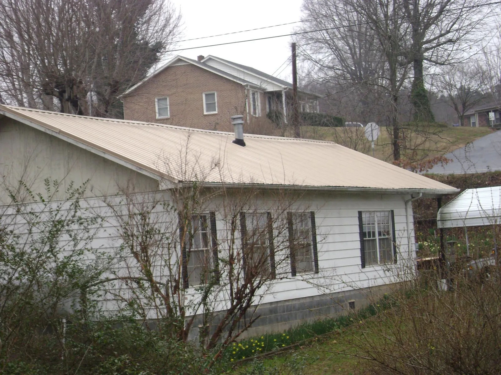 Tan metal roof on a white sided house set into a hillside — Commercial Roofing by Roofing Brothers in Burgettstown